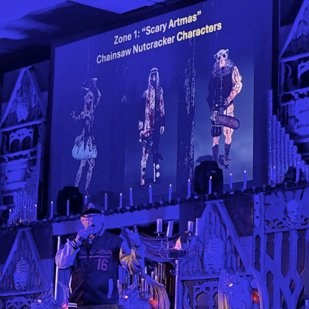 John Murdy on stage at Midsummer Scream with character concept art projected behind him