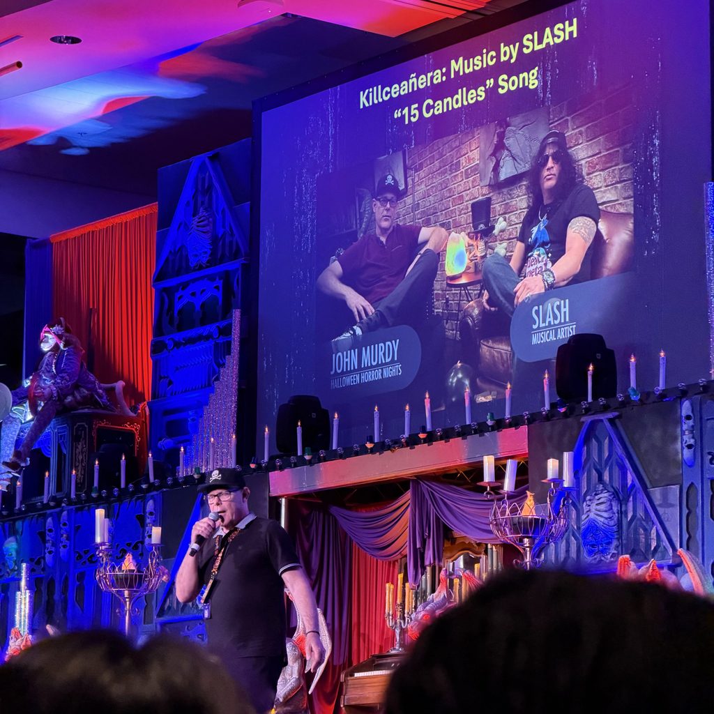 John Murdy on stage at Midsummer Scream with picture of him and Slash featured on the screen behind him