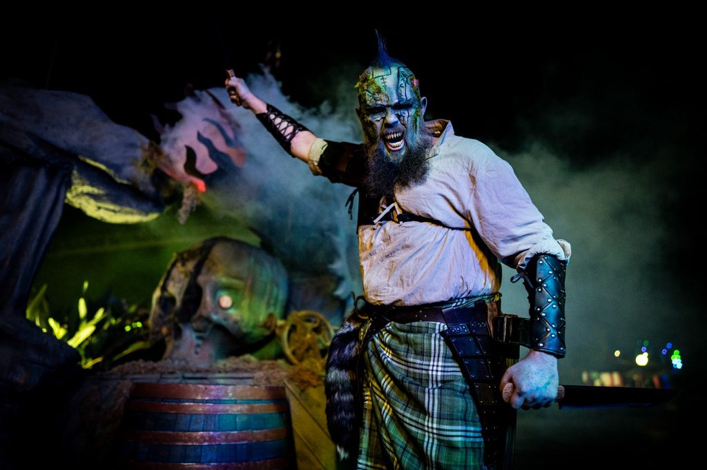 sea monster scare actor poses with skull and barrels with his fist in the air.