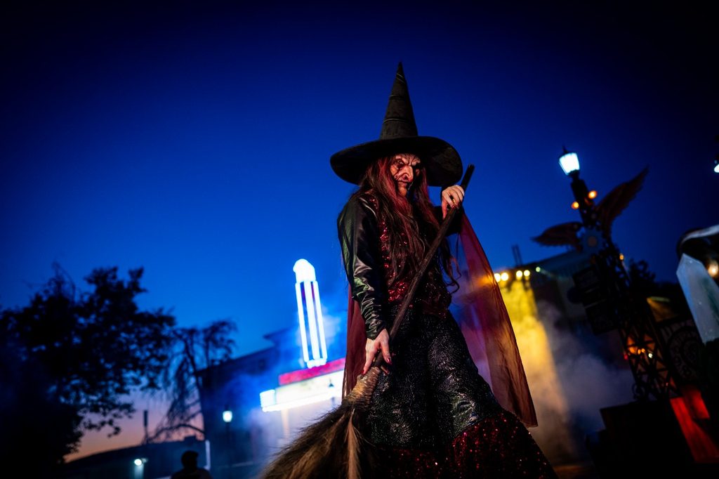 wicked witch scare actor poses with broom, looking menacingly down at the camera